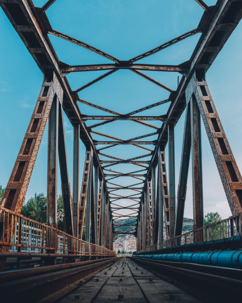 Steel railway bridge structure representing bridging finance and property funding solutions, with train tracks leading into the distance beneath a clear blue sky.